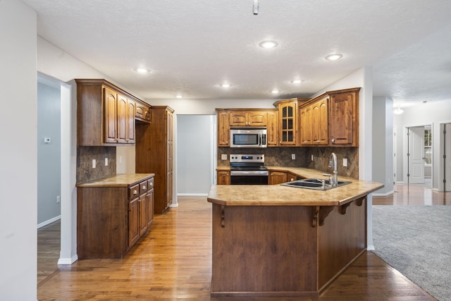 kitchen featuring a sink, stainless steel appliances, light wood-style floors, a peninsula, and glass insert cabinets