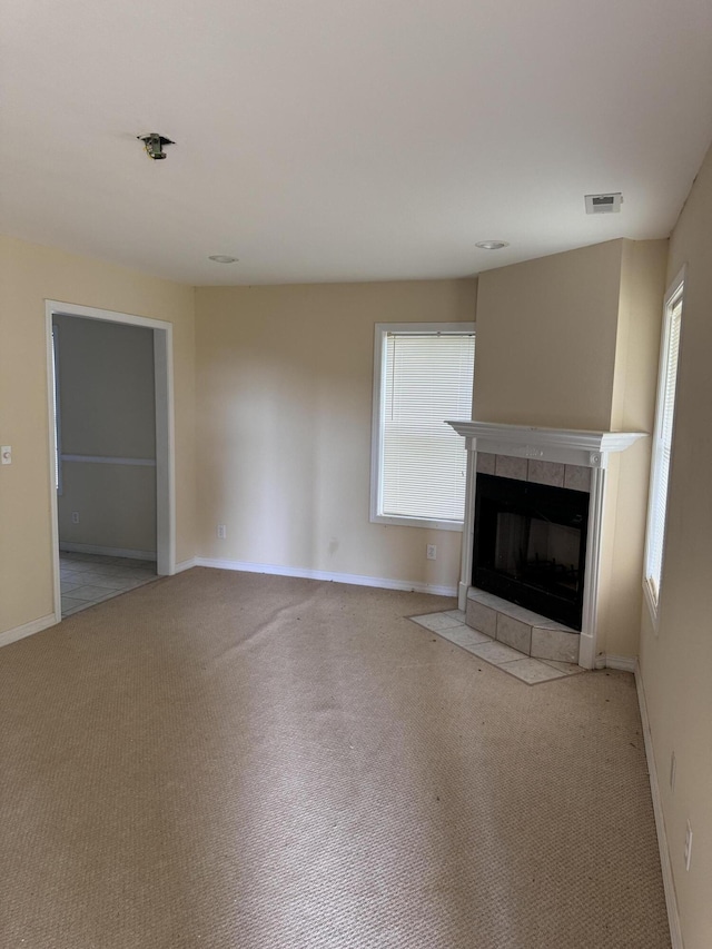 unfurnished living room with a tiled fireplace, carpet, baseboards, and visible vents