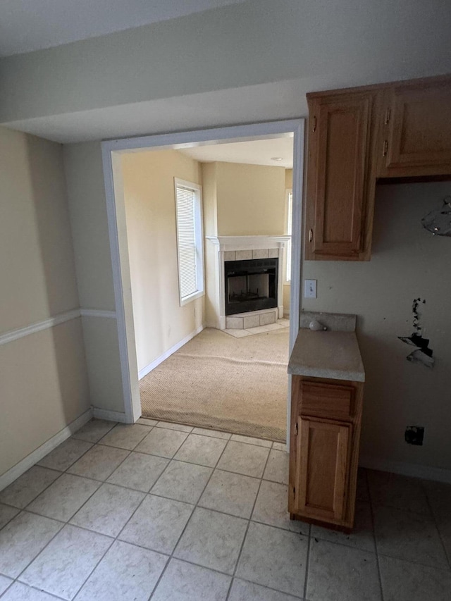 kitchen featuring baseboards, light colored carpet, light countertops, and a tile fireplace