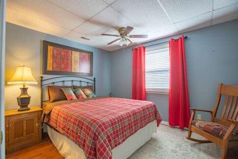 bedroom with a drop ceiling, light wood-style flooring, and a ceiling fan