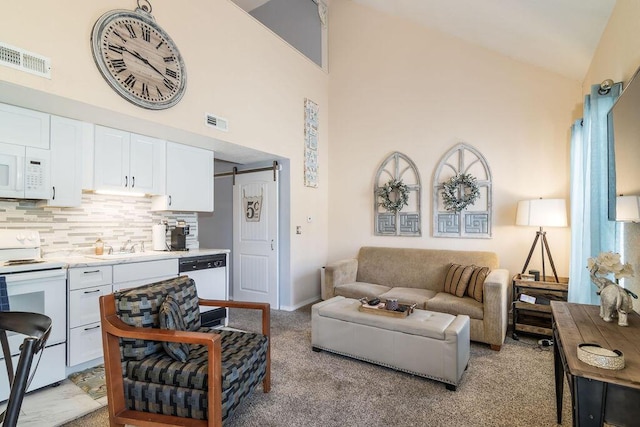 living area featuring a barn door, light carpet, visible vents, and high vaulted ceiling