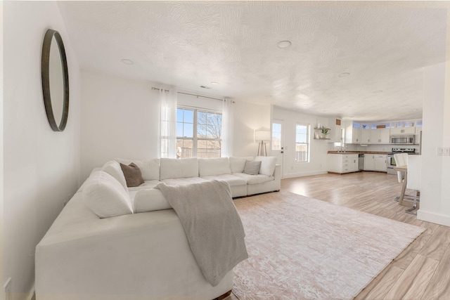 living area with baseboards, a textured ceiling, and light wood finished floors