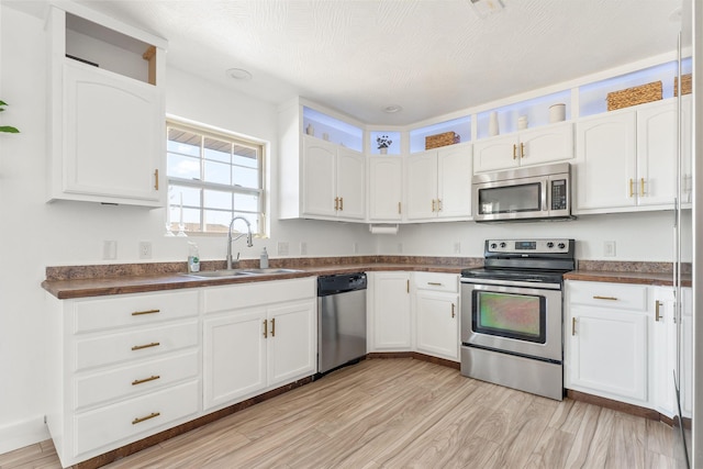 kitchen with a sink, dark countertops, appliances with stainless steel finishes, and white cabinetry