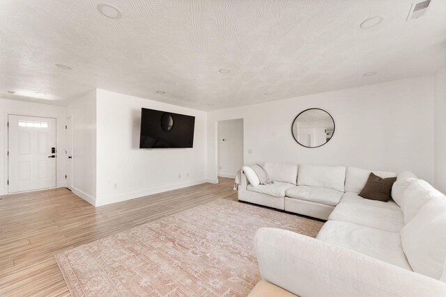 living area featuring visible vents, baseboards, light wood finished floors, and a textured ceiling