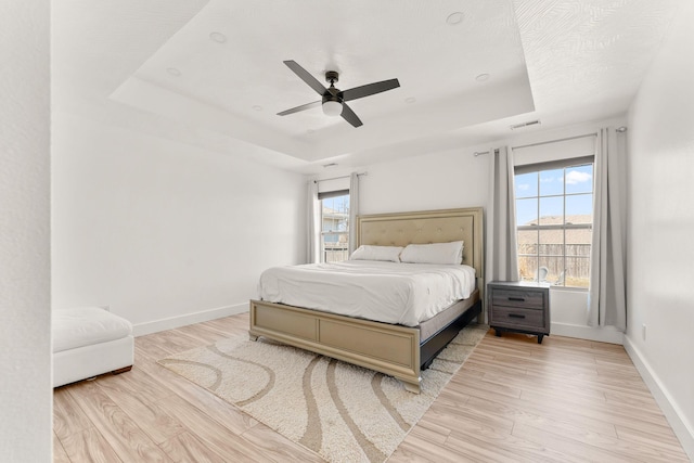 bedroom featuring a raised ceiling, light wood-style flooring, baseboards, and visible vents