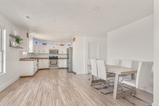 kitchen featuring visible vents, baseboards, light wood-style flooring, appliances with stainless steel finishes, and white cabinetry