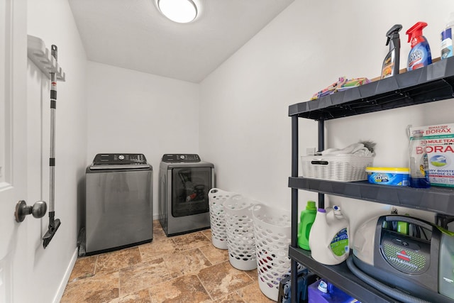 clothes washing area featuring washer and clothes dryer, laundry area, stone finish flooring, and baseboards