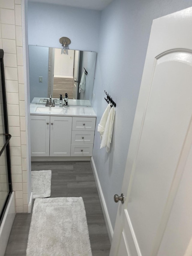 bathroom with enclosed tub / shower combo, vanity, and wood finished floors