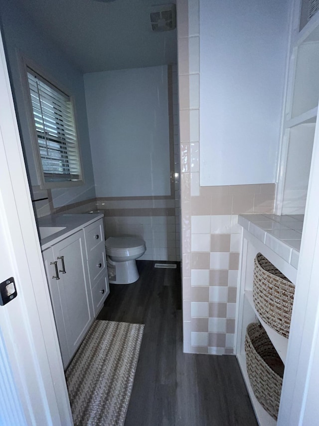 bathroom featuring a wainscoted wall, toilet, wood finished floors, tile walls, and vanity