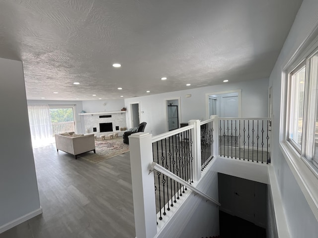 stairs with a fireplace with raised hearth, a textured ceiling, wood finished floors, recessed lighting, and baseboards