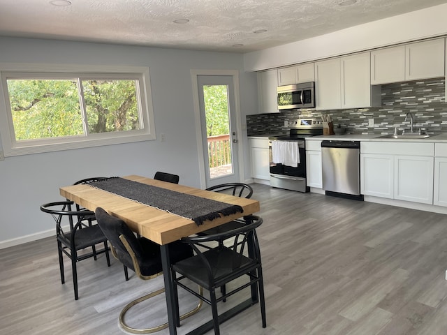 dining space with light wood-style flooring, a textured ceiling, and baseboards