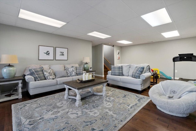 living room featuring stairway, wood finished floors, baseboards, and a drop ceiling