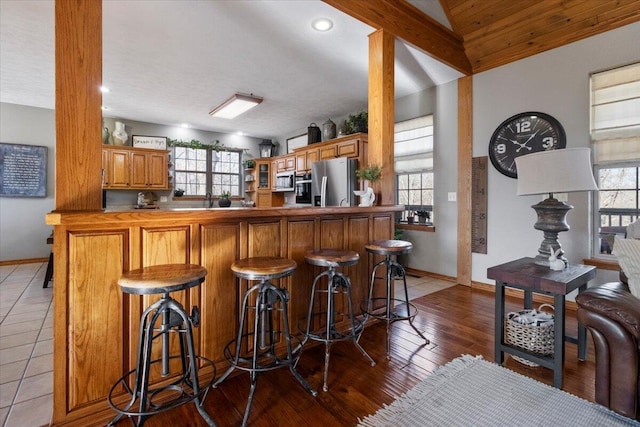 bar featuring hardwood / wood-style flooring, baseboards, appliances with stainless steel finishes, and vaulted ceiling