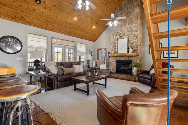 living area featuring high vaulted ceiling, wood finished floors, stairway, a stone fireplace, and wooden ceiling