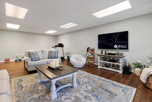 living room featuring a drop ceiling, baseboards, and wood finished floors