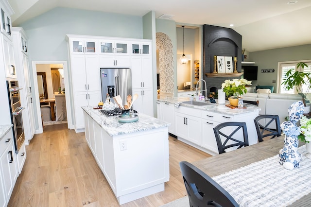 kitchen featuring a kitchen island, light wood-type flooring, vaulted ceiling, stainless steel appliances, and a sink