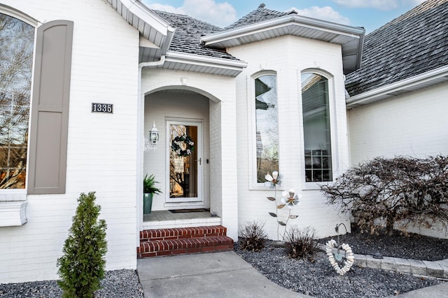 entrance to property featuring brick siding and roof with shingles