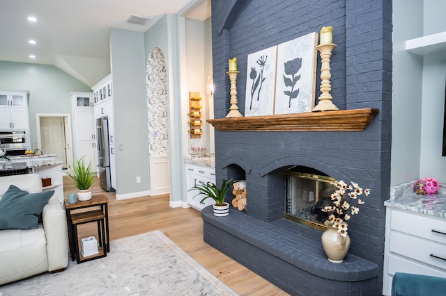 living area featuring visible vents, light wood-type flooring, lofted ceiling, recessed lighting, and a fireplace