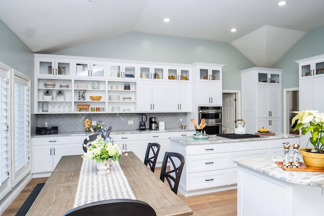 kitchen with lofted ceiling, light wood-type flooring, open shelves, and stainless steel double oven