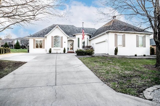 french country home featuring a high end roof, concrete driveway, a front yard, stucco siding, and an attached garage