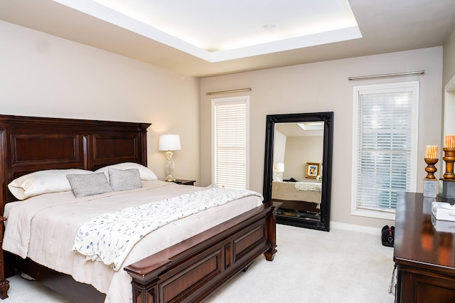 bedroom featuring a tray ceiling, light colored carpet, and baseboards