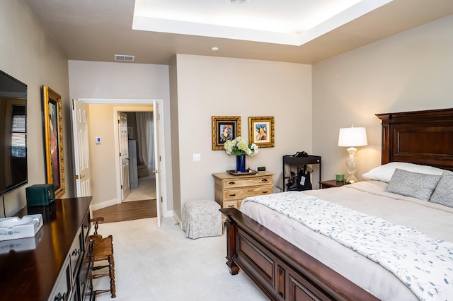 bedroom with visible vents, baseboards, light colored carpet, and a raised ceiling