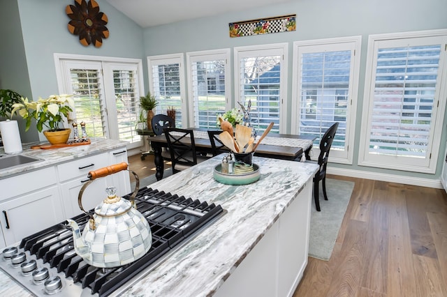 kitchen featuring lofted ceiling, wood finished floors, stainless steel gas stovetop, white cabinets, and light stone countertops