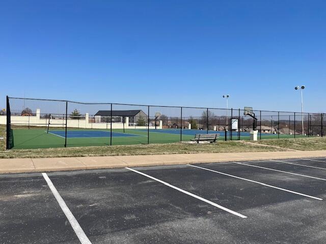 view of tennis court with community basketball court and fence