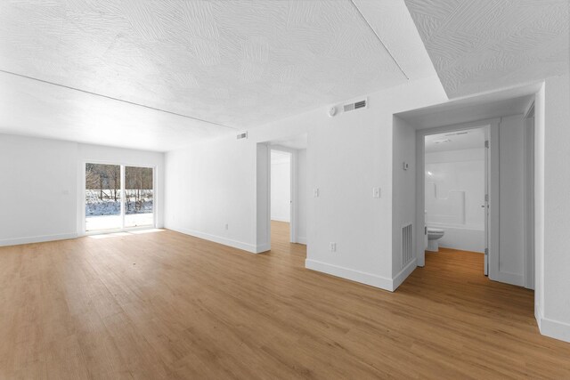 unfurnished room featuring baseboards, light wood-style floors, visible vents, and a textured ceiling