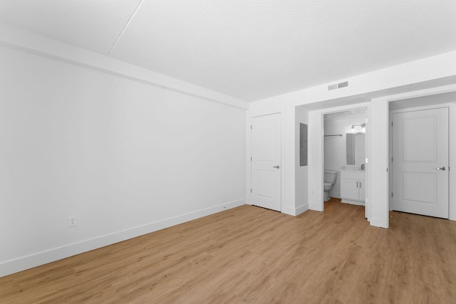 unfurnished bedroom featuring ensuite bathroom, baseboards, visible vents, and light wood finished floors