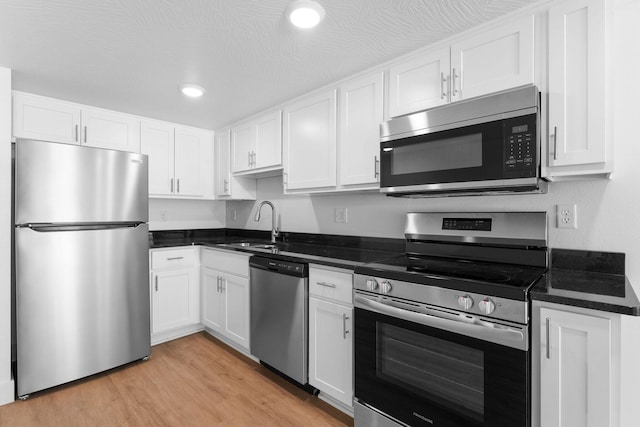 kitchen featuring light wood finished floors, a sink, white cabinets, appliances with stainless steel finishes, and dark countertops