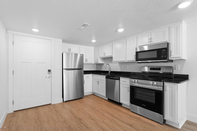 kitchen with visible vents, white cabinets, light wood-style floors, appliances with stainless steel finishes, and dark countertops