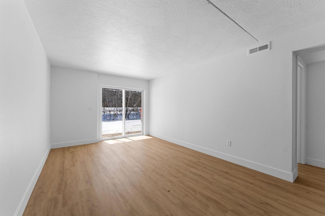 spare room featuring visible vents, light wood-style flooring, a textured ceiling, and baseboards