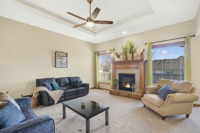 living area with a ceiling fan, baseboards, light carpet, a tiled fireplace, and a raised ceiling