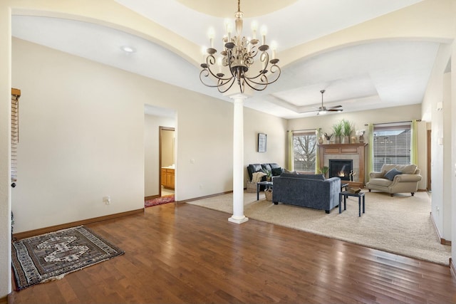 living room featuring a ceiling fan, wood finished floors, a fireplace, decorative columns, and a raised ceiling