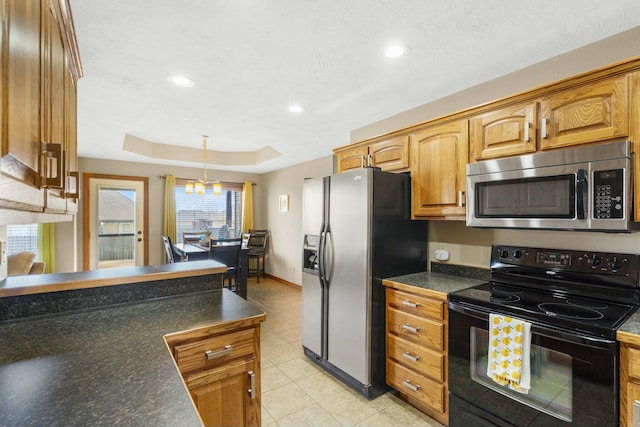 kitchen featuring brown cabinetry, dark countertops, hanging light fixtures, appliances with stainless steel finishes, and a raised ceiling