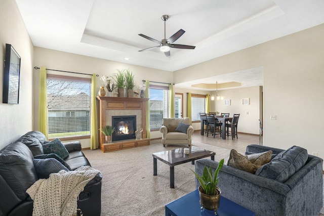 living area featuring a ceiling fan, baseboards, a tray ceiling, a tiled fireplace, and light colored carpet