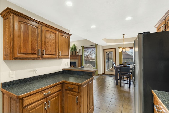 kitchen with light tile patterned floors, brown cabinets, dark countertops, and freestanding refrigerator