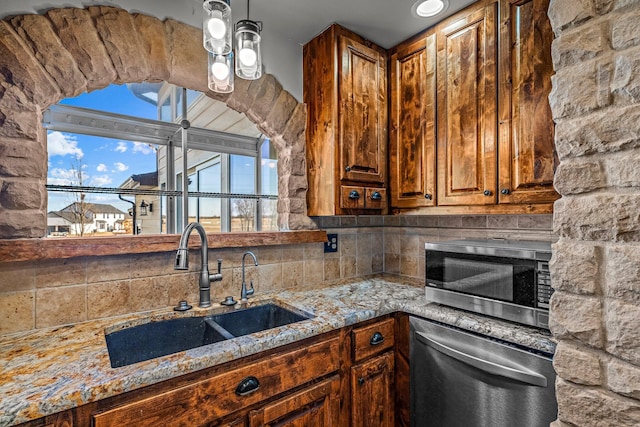 kitchen featuring brown cabinets, a sink, light stone counters, backsplash, and stainless steel appliances