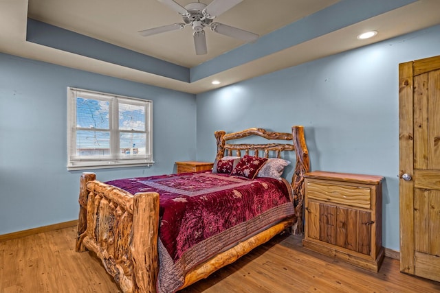 bedroom with recessed lighting, baseboards, a raised ceiling, and wood finished floors