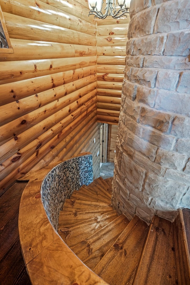 stairway featuring hardwood / wood-style flooring, a notable chandelier, and rustic walls