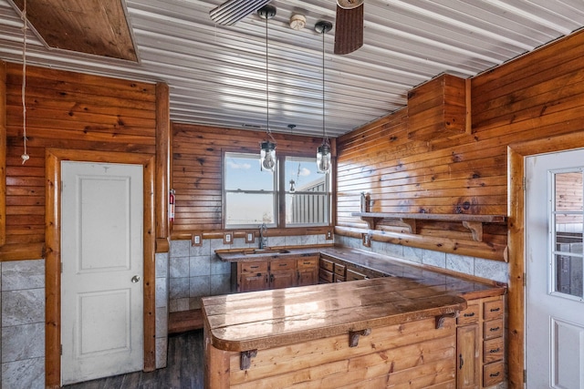 kitchen with a sink, dark countertops, a peninsula, ceiling fan, and hanging light fixtures