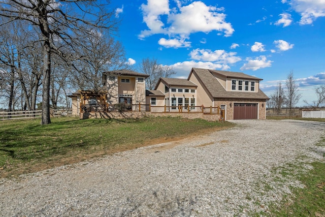 view of front of house with gravel driveway, a front lawn, fence, and a garage