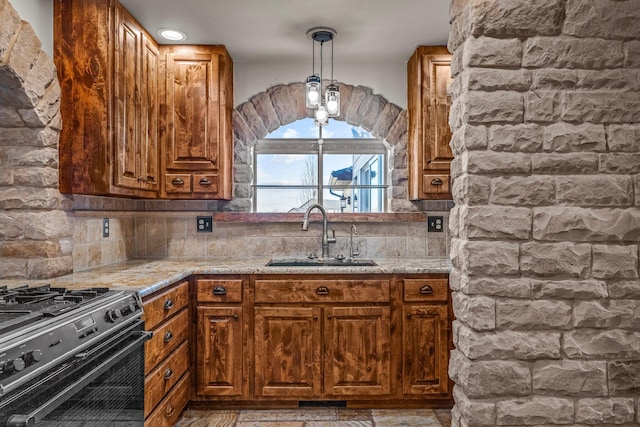 kitchen featuring brown cabinetry, stainless steel range with gas stovetop, a sink, decorative light fixtures, and backsplash