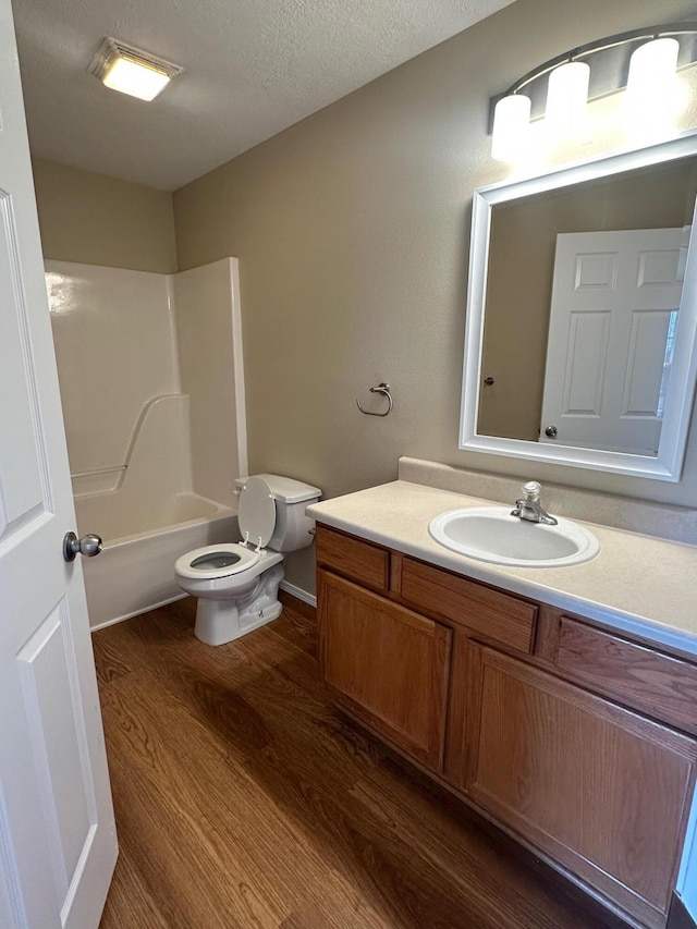 bathroom with toilet, a textured ceiling, wood finished floors, washtub / shower combination, and vanity