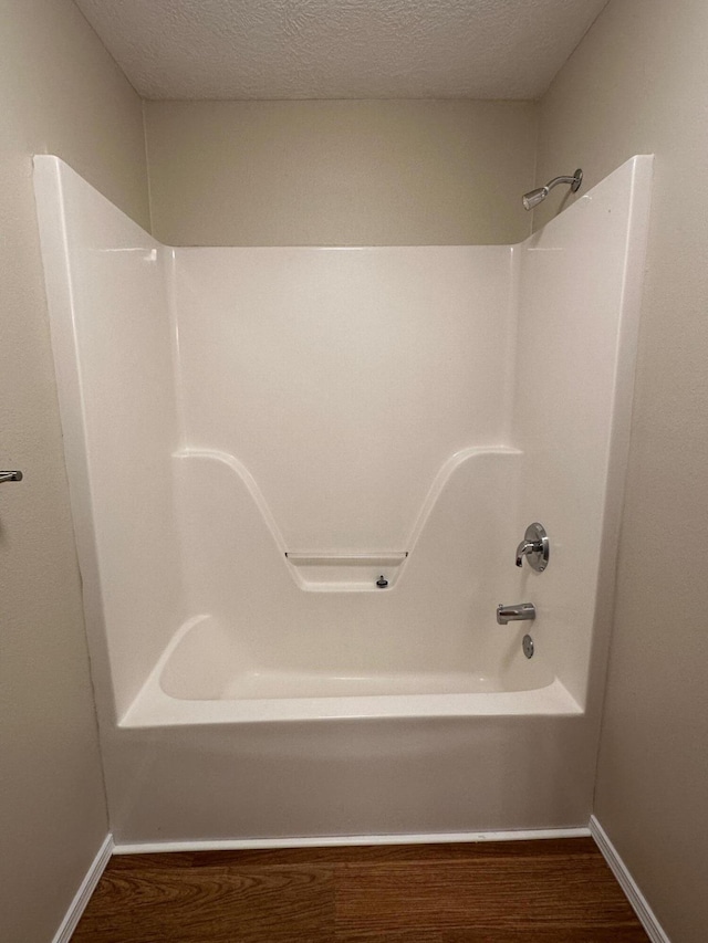 bathroom with a textured ceiling, bathing tub / shower combination, baseboards, and wood finished floors