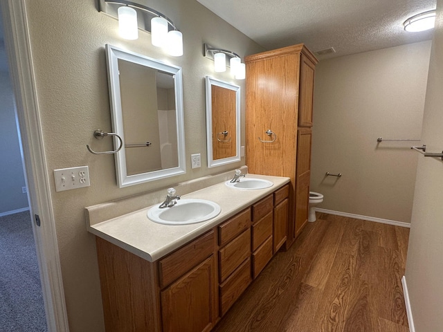 full bathroom featuring a textured ceiling, toilet, wood finished floors, and a sink