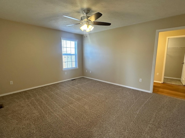 spare room with visible vents, ceiling fan, baseboards, a textured ceiling, and dark colored carpet