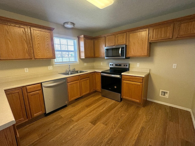 kitchen with brown cabinets, appliances with stainless steel finishes, wood finished floors, and a sink