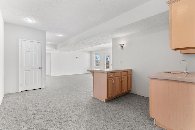 kitchen with tile counters, open floor plan, light colored carpet, a peninsula, and a sink